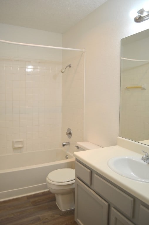 full bathroom featuring tiled shower / bath combo, hardwood / wood-style floors, a textured ceiling, toilet, and vanity