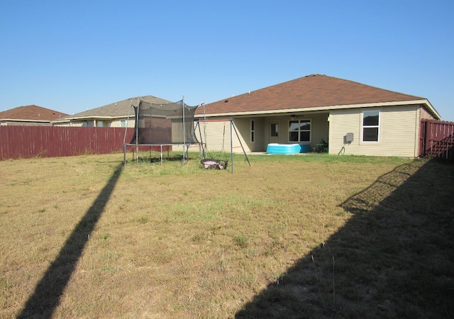 back of property featuring a lawn and a trampoline