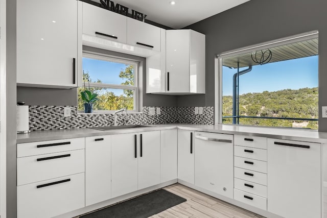 kitchen featuring sink, backsplash, white cabinets, white dishwasher, and light hardwood / wood-style floors