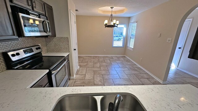 kitchen with backsplash, a textured ceiling, stainless steel appliances, an inviting chandelier, and hanging light fixtures