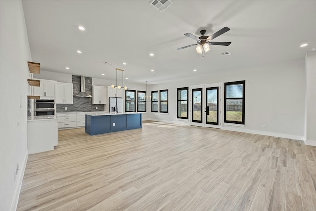 kitchen featuring pendant lighting, white cabinets, wall chimney range hood, an island with sink, and light hardwood / wood-style floors