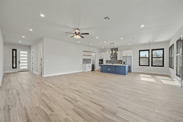 unfurnished living room featuring ceiling fan, sink, and light wood-type flooring