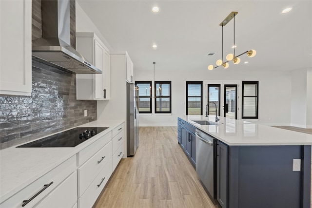 kitchen featuring sink, wall chimney exhaust hood, stainless steel appliances, decorative light fixtures, and white cabinets