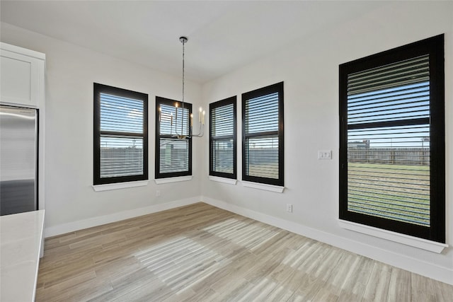 unfurnished dining area with a chandelier and light wood-type flooring