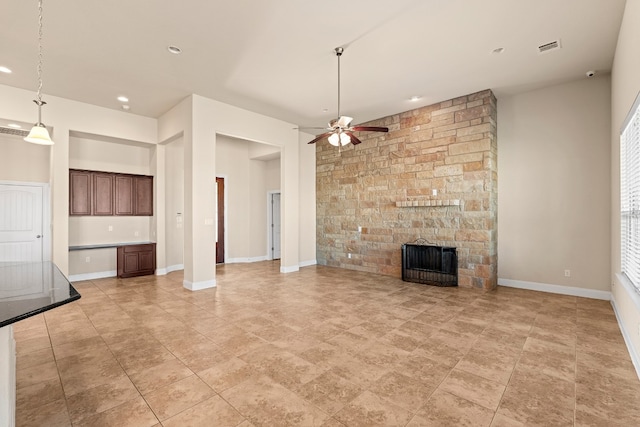 unfurnished living room featuring ceiling fan and a stone fireplace