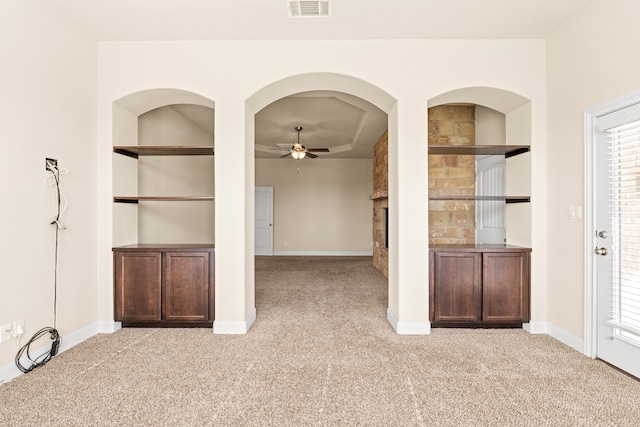 interior space with ceiling fan, a stone fireplace, built in features, and light carpet