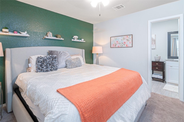 bedroom with ensuite bathroom and light colored carpet