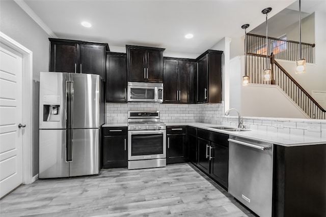 kitchen featuring light wood-type flooring, tasteful backsplash, stainless steel appliances, sink, and hanging light fixtures