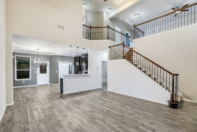 unfurnished living room with a chandelier, hardwood / wood-style floors, a towering ceiling, and ornamental molding