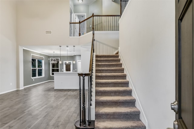 staircase with a chandelier, wood-type flooring, and a high ceiling