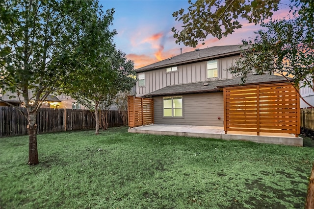 back house at dusk featuring a lawn and a patio area