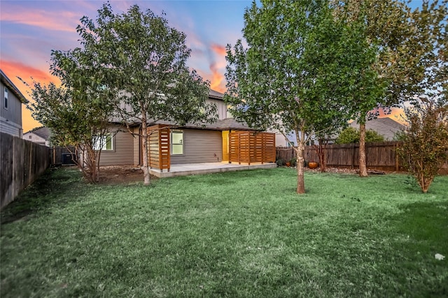 back house at dusk featuring a yard and a patio area