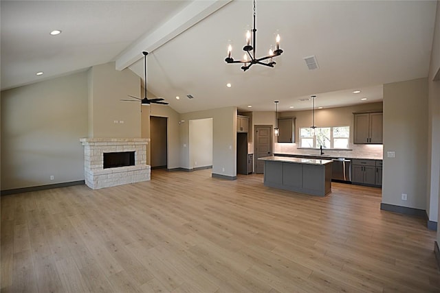 unfurnished living room with ceiling fan with notable chandelier, high vaulted ceiling, beamed ceiling, sink, and light wood-type flooring