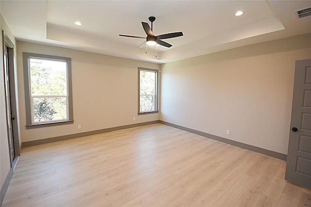 spare room featuring light hardwood / wood-style flooring, ceiling fan, and a tray ceiling