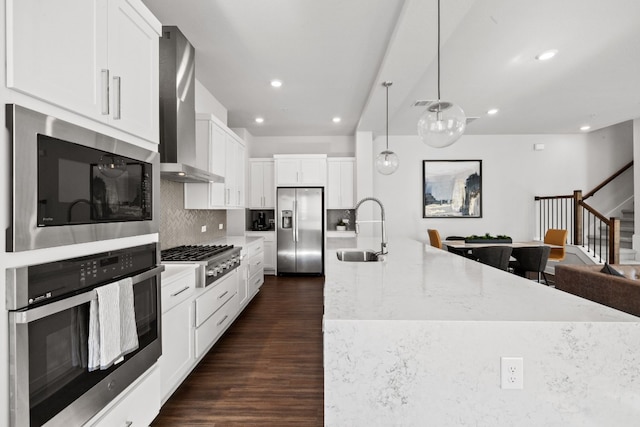 kitchen with sink, hanging light fixtures, wall chimney exhaust hood, white cabinetry, and stainless steel appliances