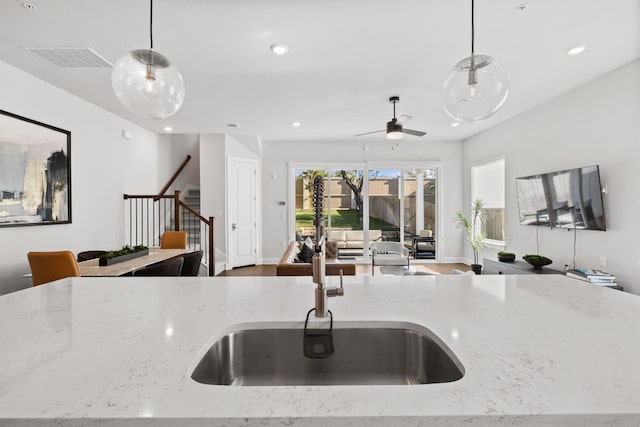 kitchen featuring ceiling fan, sink, light stone counters, pendant lighting, and hardwood / wood-style flooring