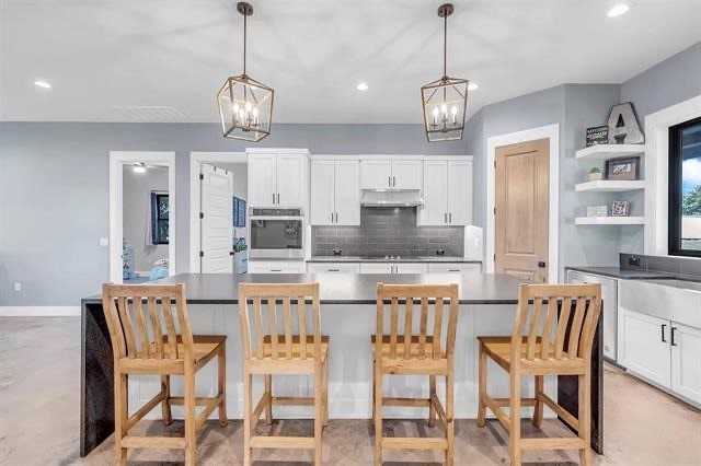 kitchen featuring backsplash, white cabinetry, hanging light fixtures, and a breakfast bar area