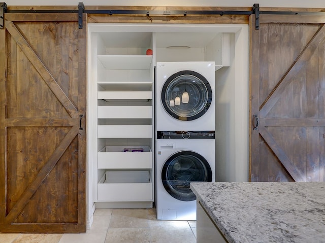 washroom with stacked washer / drying machine, a barn door, and light tile patterned floors