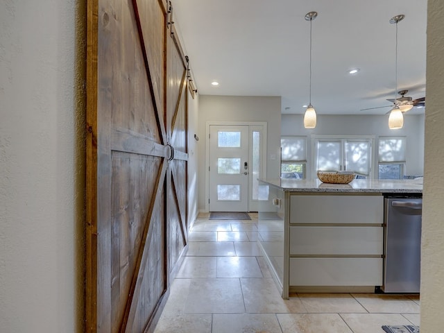 kitchen with hanging light fixtures, stainless steel dishwasher, ceiling fan, a barn door, and light stone countertops