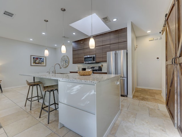 kitchen with a center island with sink, a barn door, appliances with stainless steel finishes, and pendant lighting