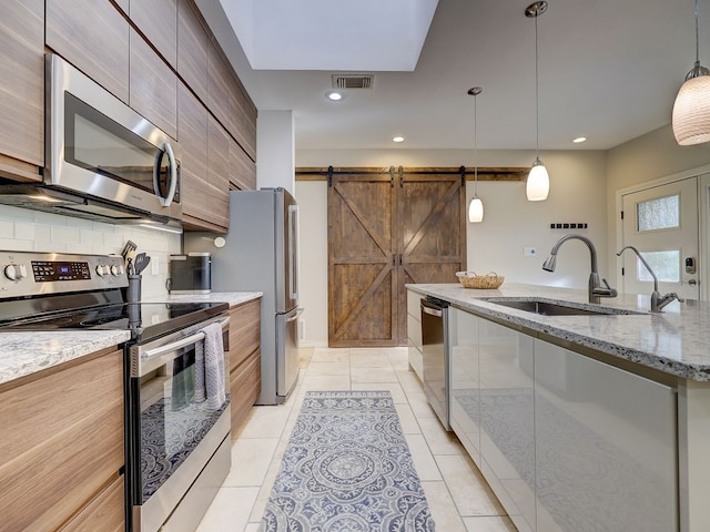 kitchen featuring pendant lighting, sink, a barn door, light tile patterned floors, and appliances with stainless steel finishes