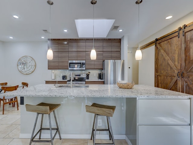 kitchen with a kitchen breakfast bar, a barn door, decorative light fixtures, decorative backsplash, and appliances with stainless steel finishes