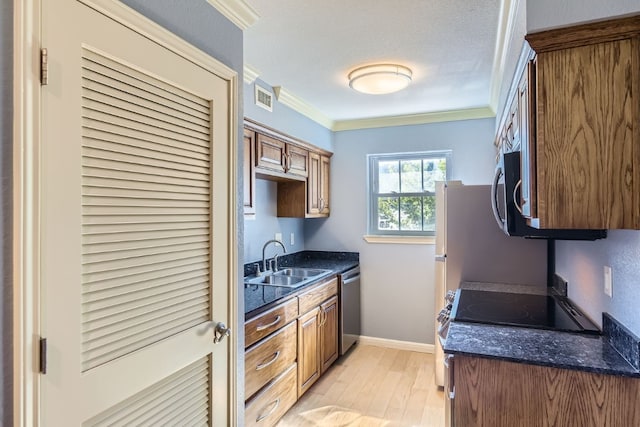 kitchen featuring ornamental molding, stainless steel appliances, sink, dark stone countertops, and light hardwood / wood-style floors