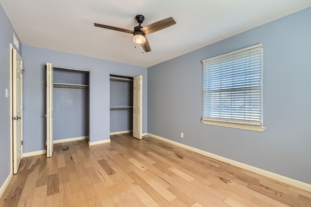 unfurnished bedroom with ceiling fan, light wood-type flooring, and multiple closets