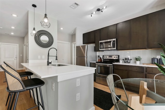 kitchen with decorative backsplash, dark brown cabinets, stainless steel appliances, sink, and light hardwood / wood-style floors