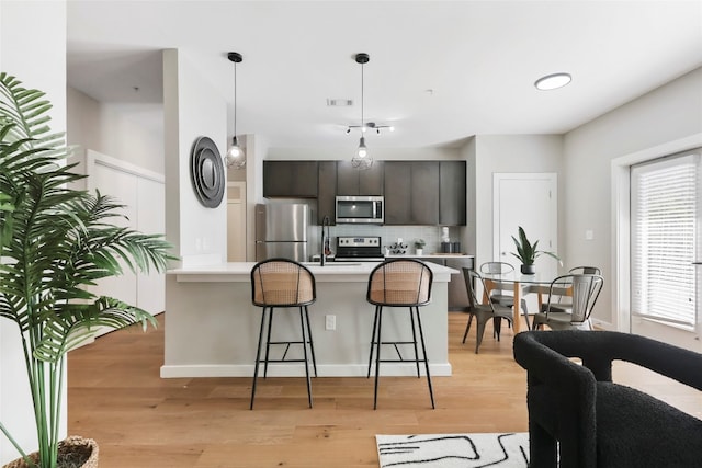 kitchen with a kitchen bar, light wood-type flooring, tasteful backsplash, dark brown cabinets, and stainless steel appliances