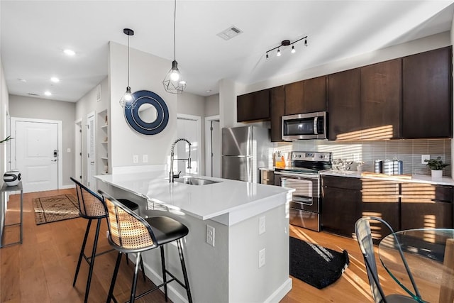 kitchen with appliances with stainless steel finishes, sink, a breakfast bar area, and light hardwood / wood-style floors