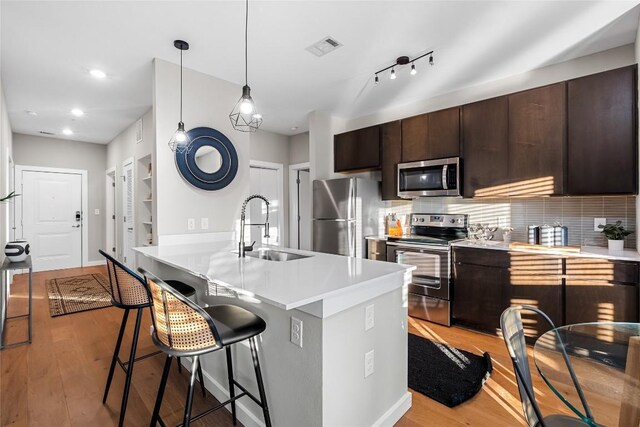 kitchen with stainless steel appliances, a sink, light countertops, light wood-style flooring, and recessed lighting