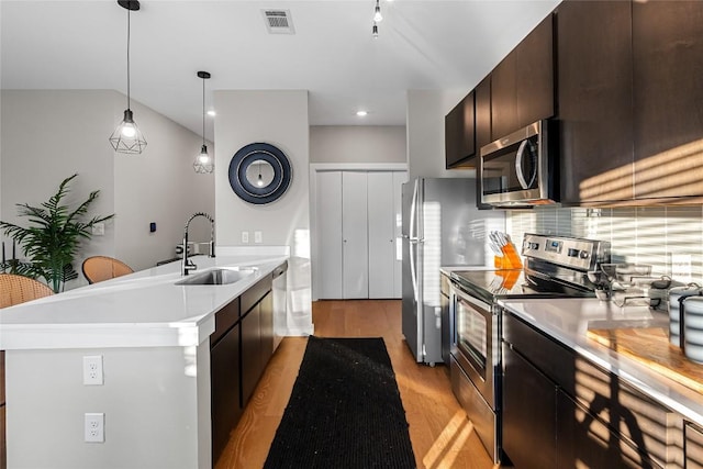 kitchen featuring decorative light fixtures, sink, dark brown cabinetry, stainless steel appliances, and light wood-type flooring