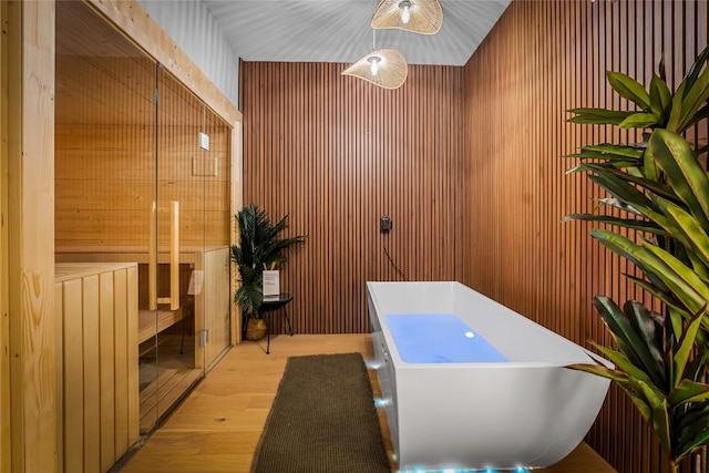 bathroom with wood-type flooring, a bath, and wooden walls