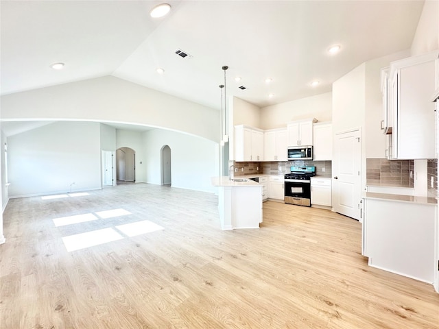 kitchen featuring white cabinetry, light hardwood / wood-style flooring, lofted ceiling, decorative backsplash, and appliances with stainless steel finishes