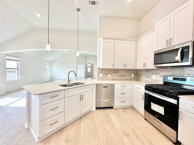 kitchen with lofted ceiling, sink, appliances with stainless steel finishes, decorative light fixtures, and kitchen peninsula