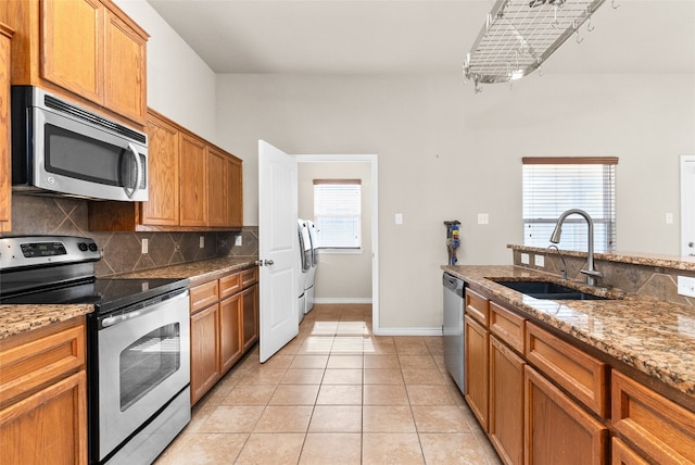 kitchen featuring light stone countertops, backsplash, stainless steel appliances, sink, and light tile patterned flooring