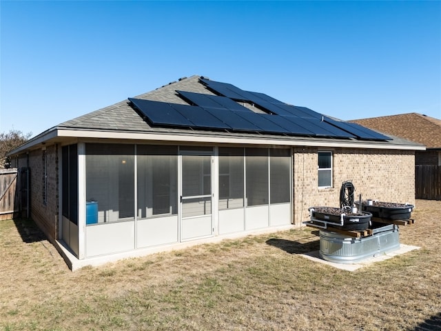 back of property with a sunroom, a yard, and solar panels