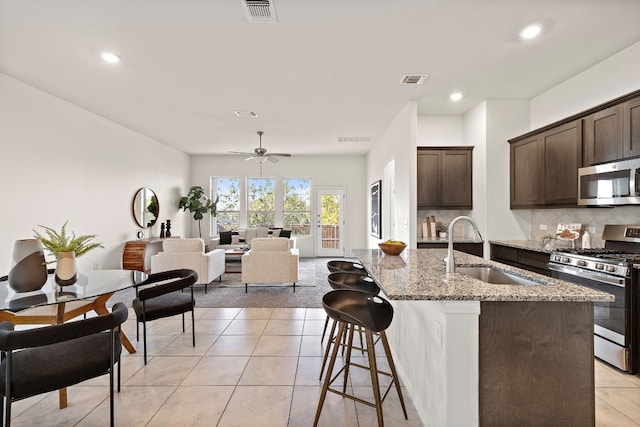 kitchen featuring a kitchen island with sink, sink, light tile patterned floors, appliances with stainless steel finishes, and light stone counters