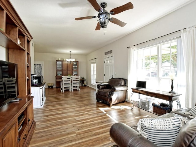 living room featuring ceiling fan with notable chandelier and light hardwood / wood-style flooring