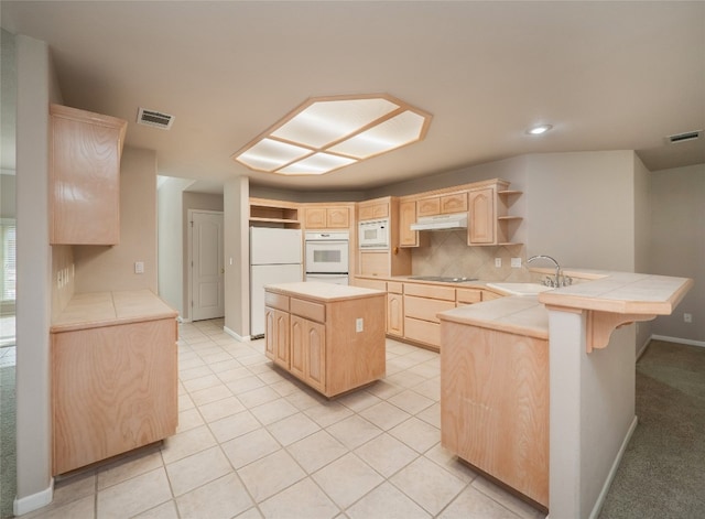 kitchen with kitchen peninsula, white appliances, sink, light brown cabinets, and tile countertops