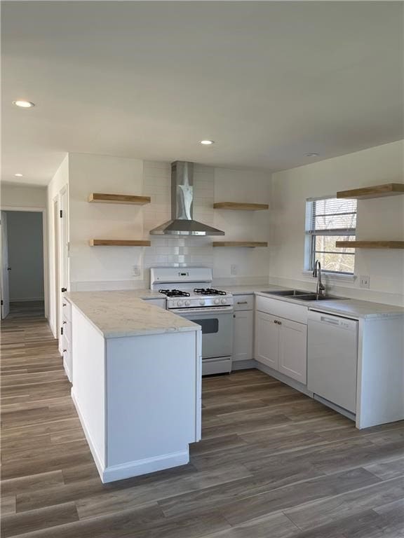 kitchen featuring white appliances, dark wood-type flooring, wall chimney range hood, sink, and white cabinetry