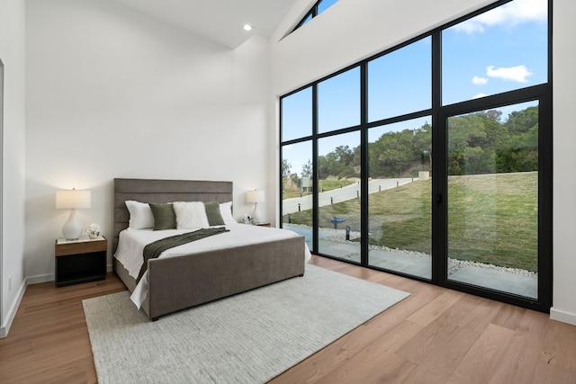 bedroom with multiple windows, hardwood / wood-style floors, a high ceiling, and access to exterior