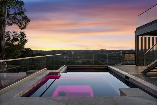 pool at dusk featuring an in ground hot tub