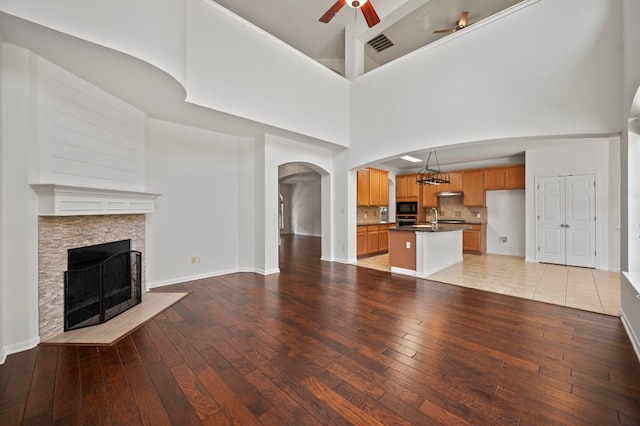 unfurnished living room featuring high vaulted ceiling, ceiling fan with notable chandelier, a stone fireplace, sink, and light hardwood / wood-style flooring