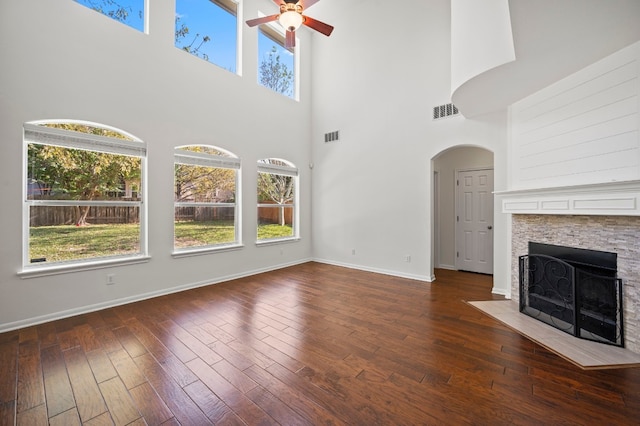 unfurnished living room featuring a fireplace, ceiling fan, dark wood-type flooring, and a high ceiling