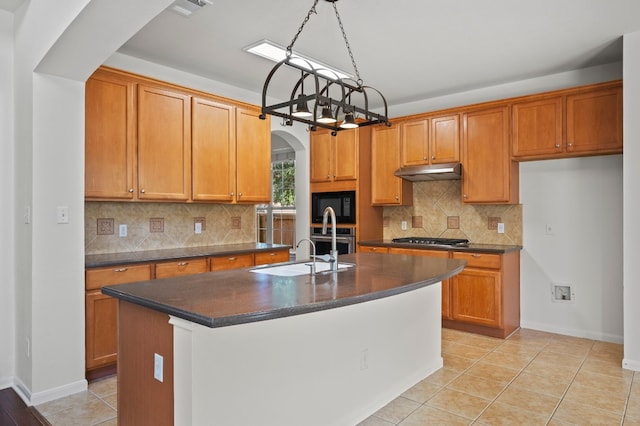 kitchen featuring a center island with sink, sink, decorative backsplash, light tile patterned floors, and stainless steel appliances