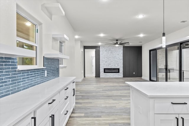 kitchen featuring ceiling fan, a fireplace, white cabinetry, and hanging light fixtures