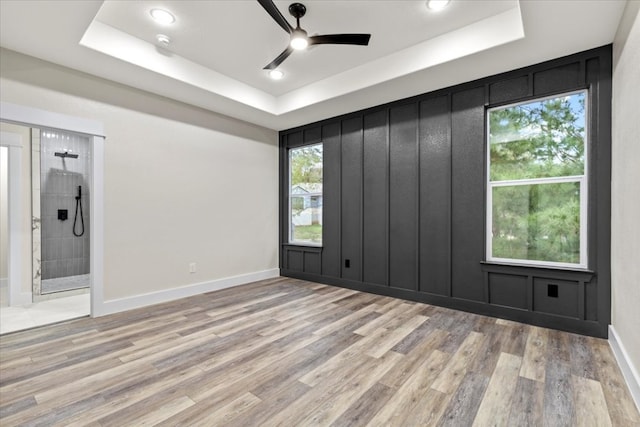 empty room featuring a raised ceiling, ceiling fan, and light wood-type flooring