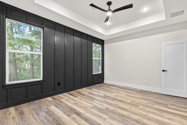 unfurnished room with a raised ceiling, ceiling fan, and light hardwood / wood-style flooring